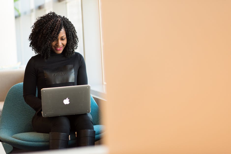 A person with curly hair and a black top is sitting on a chair, using a laptop, smiling against a light background, likely building a high-quality email list to enhance the effectiveness of their email campaigns.