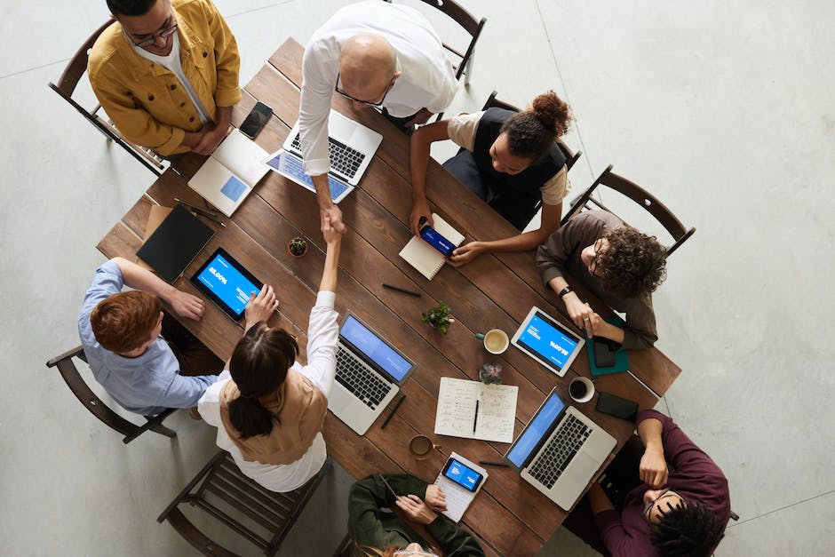 Top view of seven people around a table, each with a laptop, engaged in discussion with two individuals shaking hands, suggesting a collaborative meeting environment focused on email segmentation and marketing analytics.